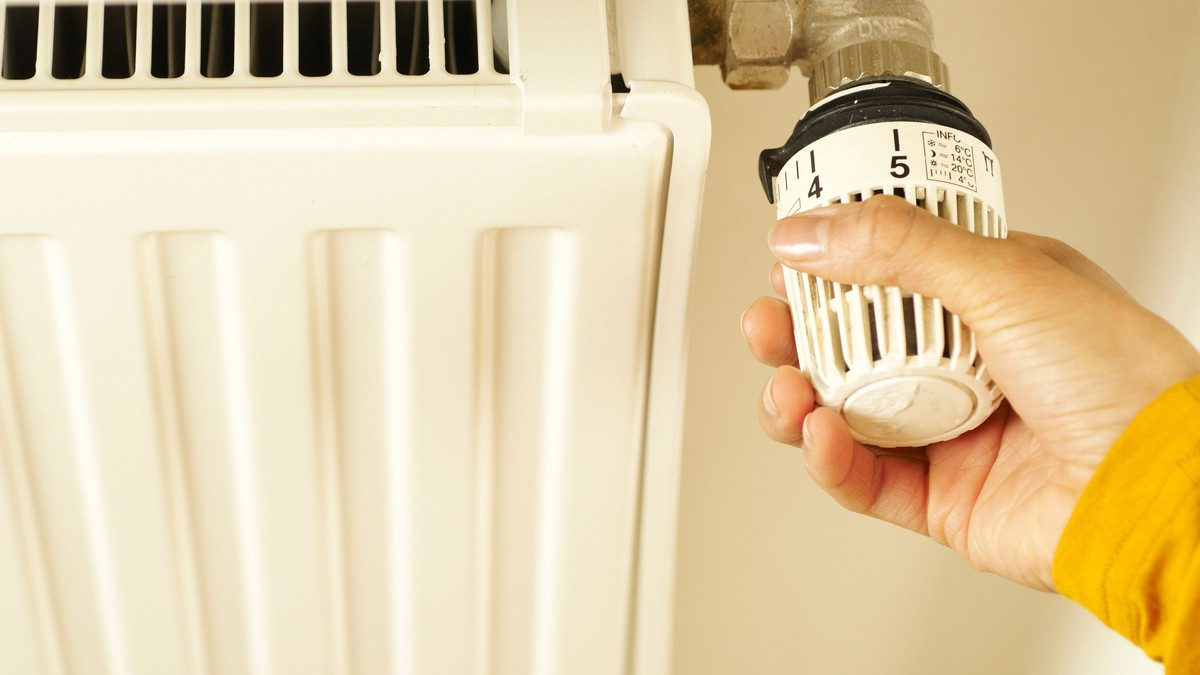 Main réglant la tête thermostatique d’un radiateur blanc