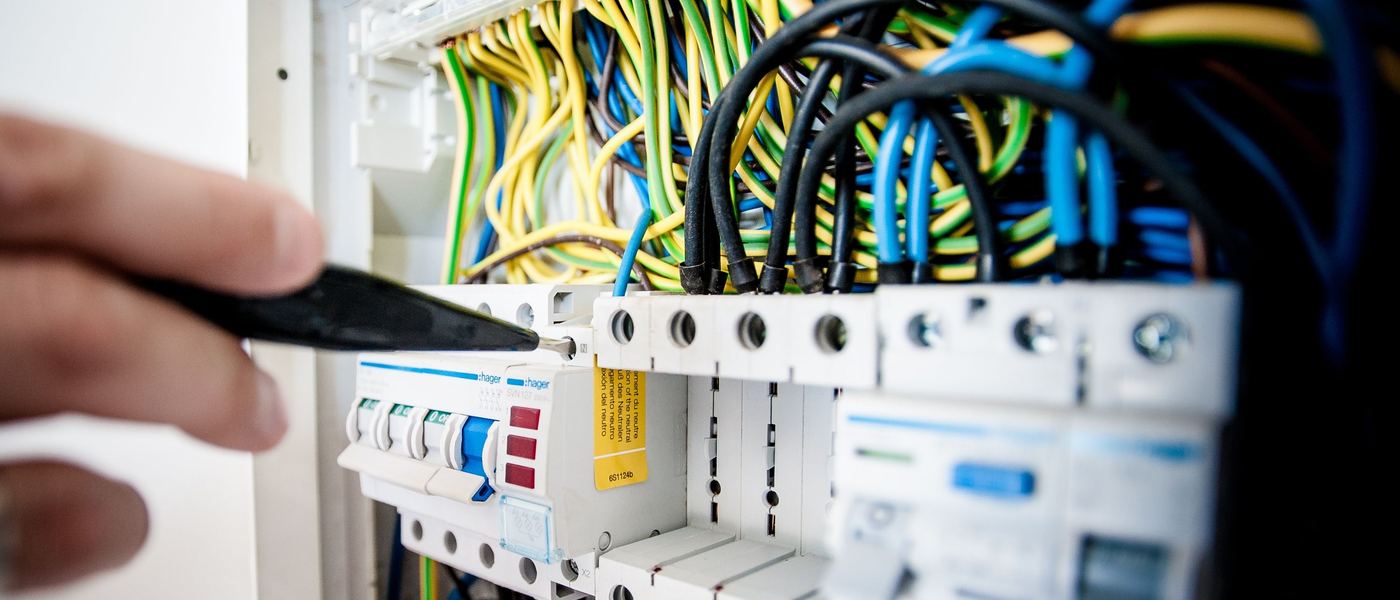 Main d’électricien testant un disjoncteur dans un tableau électrique ouvert et câblé