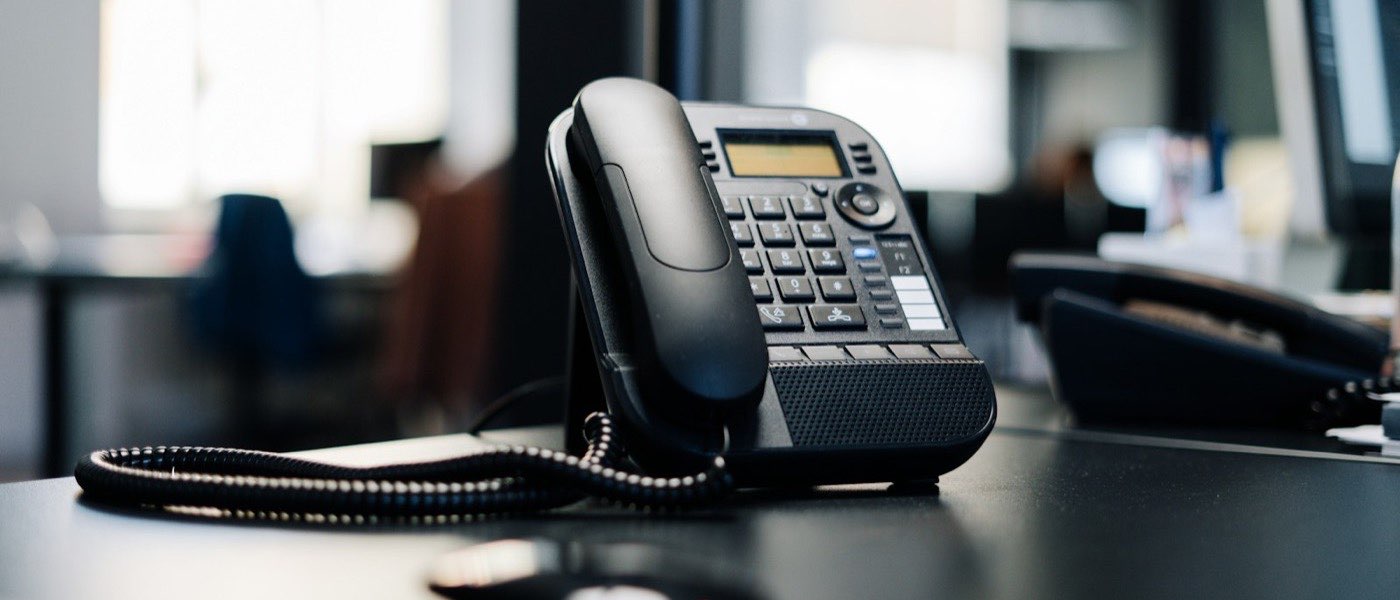 Téléphone de bureau à combiné posé sur un plan de travail noir, dans un open space