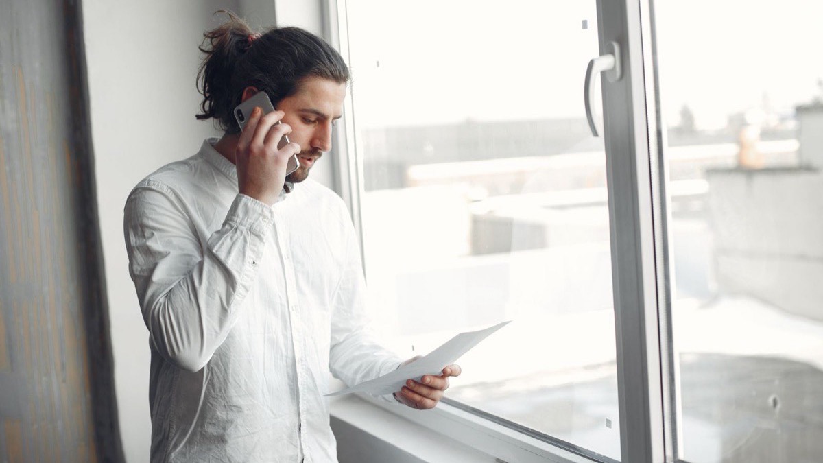 Un professionnel au téléphone près d’une fenêtre, un document à la main