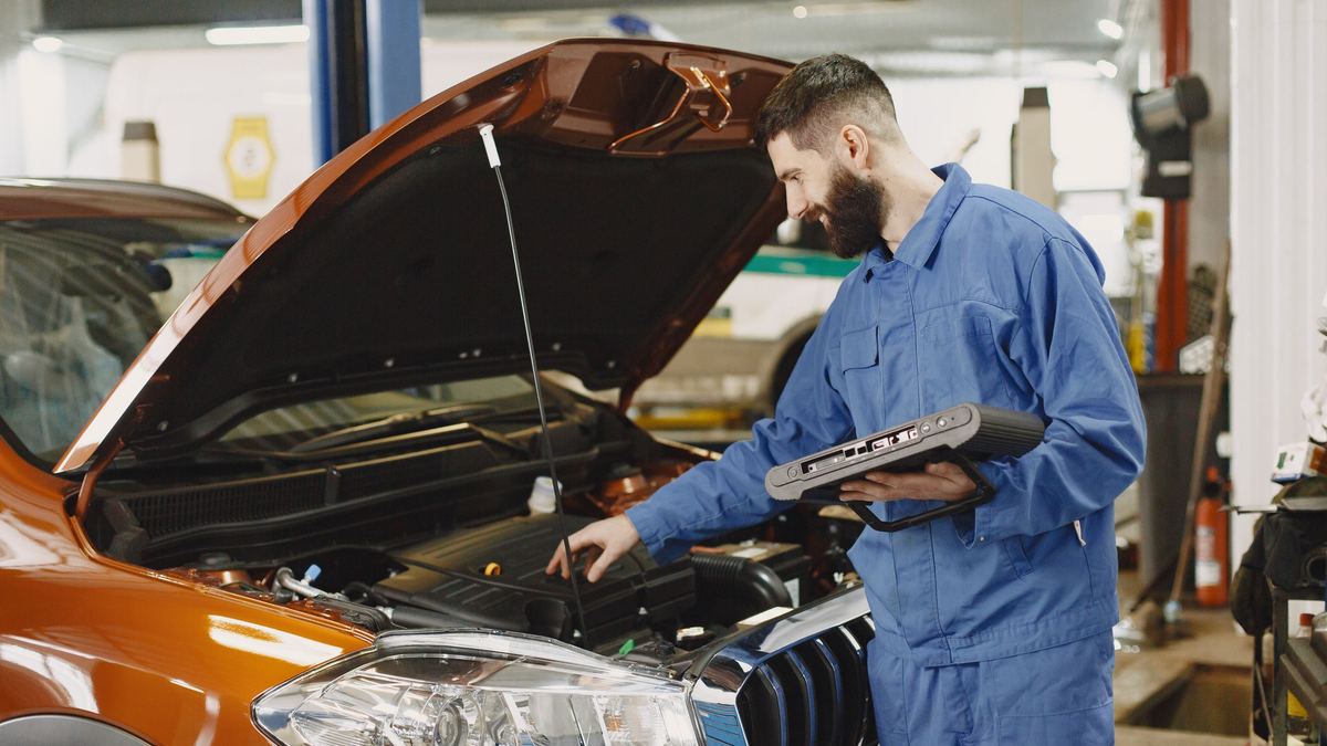 Mécanicien penché sur un moteur, capot ouvert, une valise de diagnostic à la main