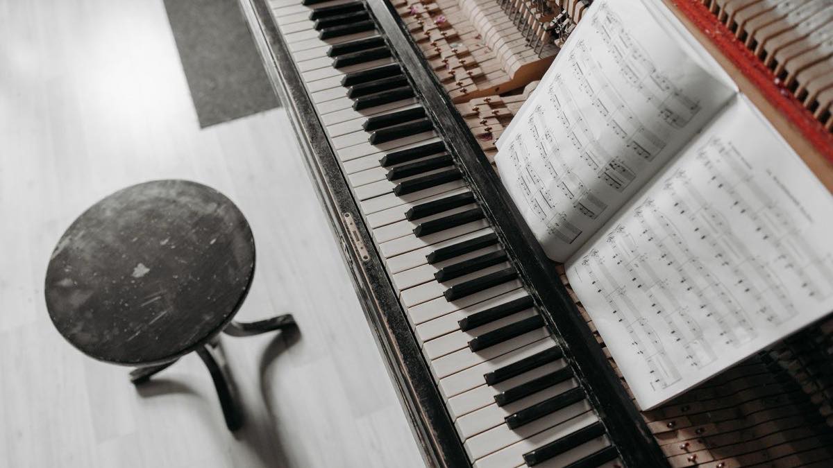 Partition ouverte posée sur un piano droit, un tabouret de pianiste à côté