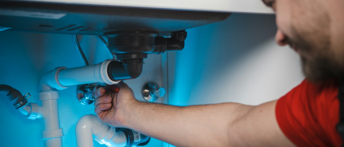 Plombier en intervention sous un évier, sur le siphon et les canalisations
