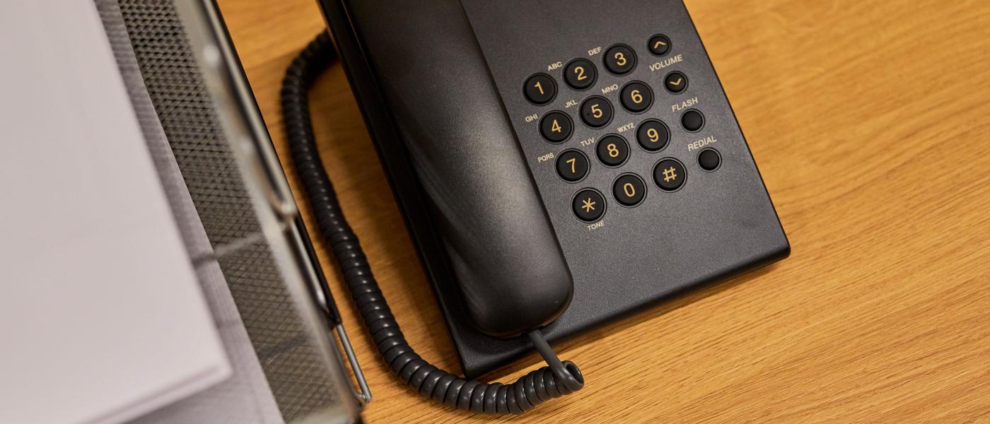 Téléphone fixe noir posé sur un bureau en bois à côté d’un classeur