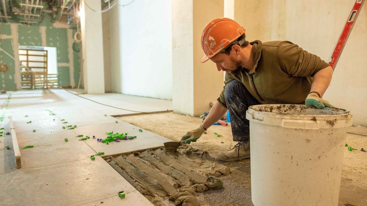 Carreleur casqué posant un carreau sur un lit de colle dans un chantier en rénovation