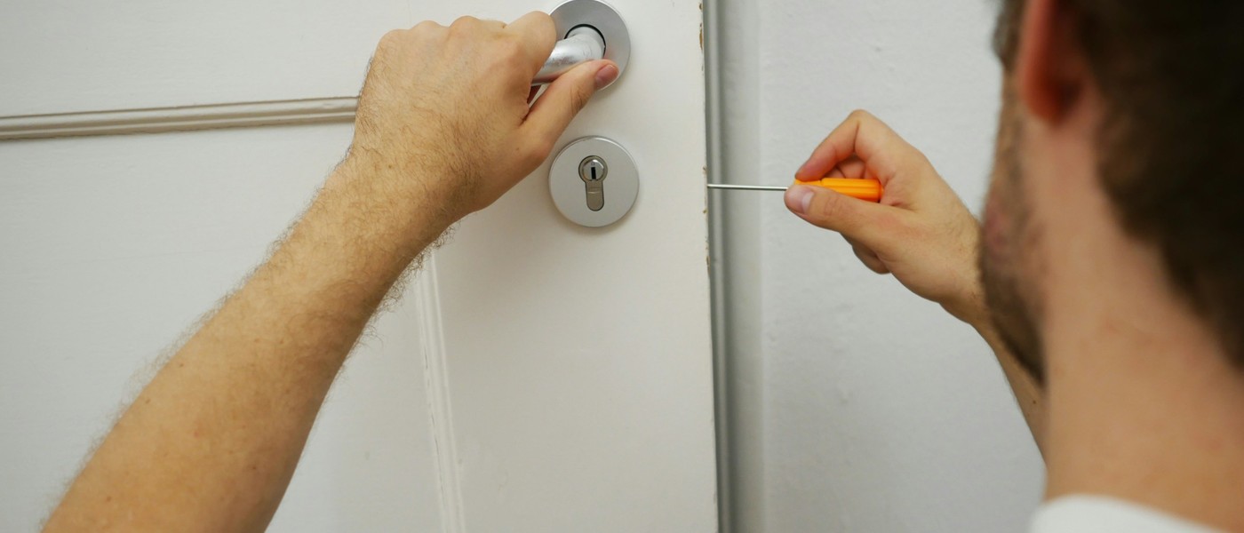 Serrurier tenant la poignée d’une porte d’entrée blanche et travaillant sur le cylindre avec un tournevis