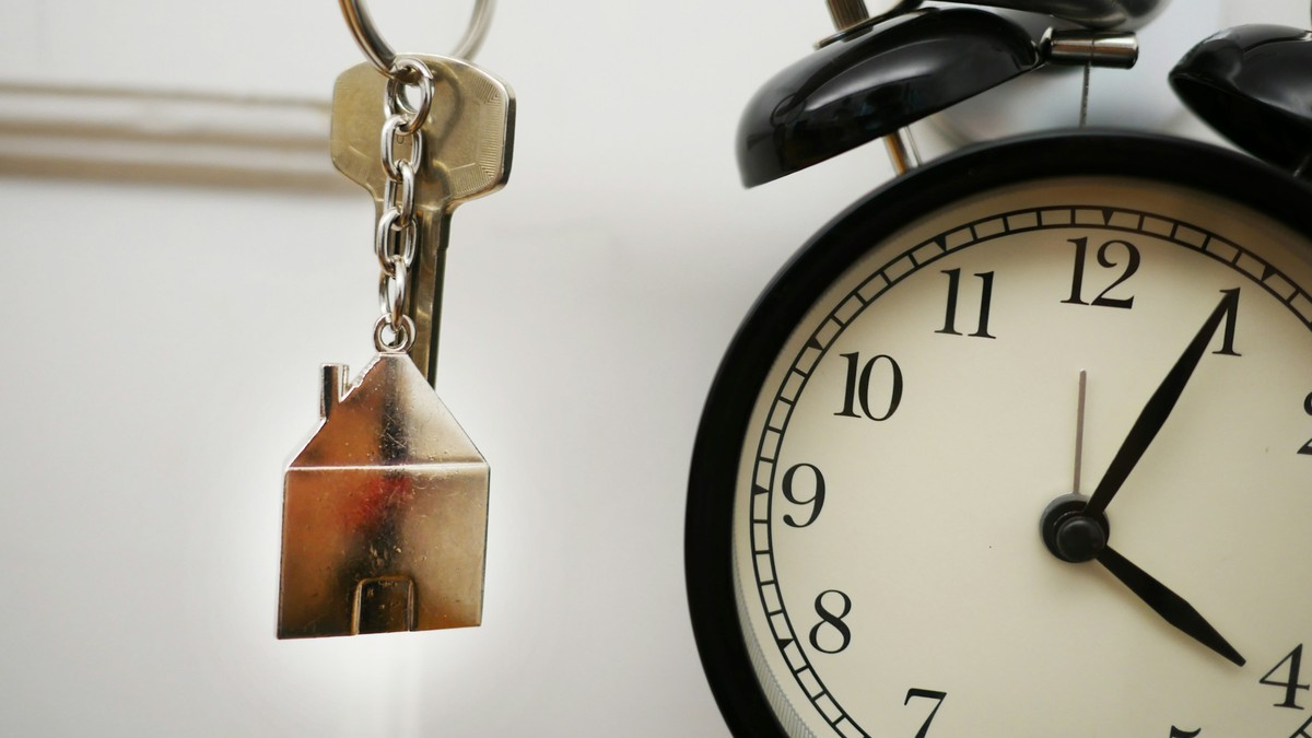Clé à porte-clés en forme de maison à côté d’un réveil indiquant quatre heures