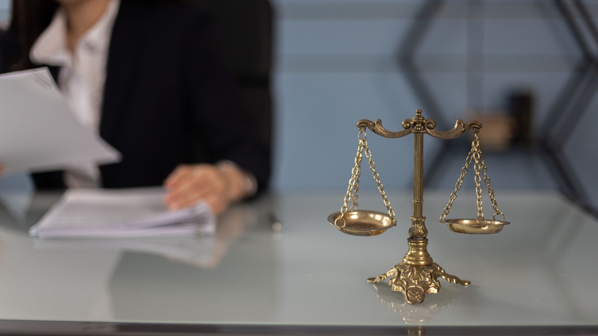 Balance de la justice en laiton sur un bureau, une avocate consultant un dossier en arrière-plan