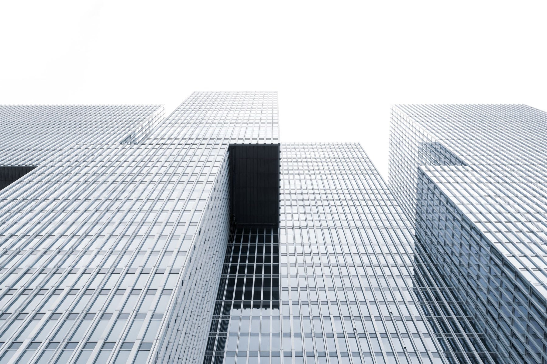 Trois tours de bureaux en verre photographiées depuis le sol, façades claires sur un ciel blanc.